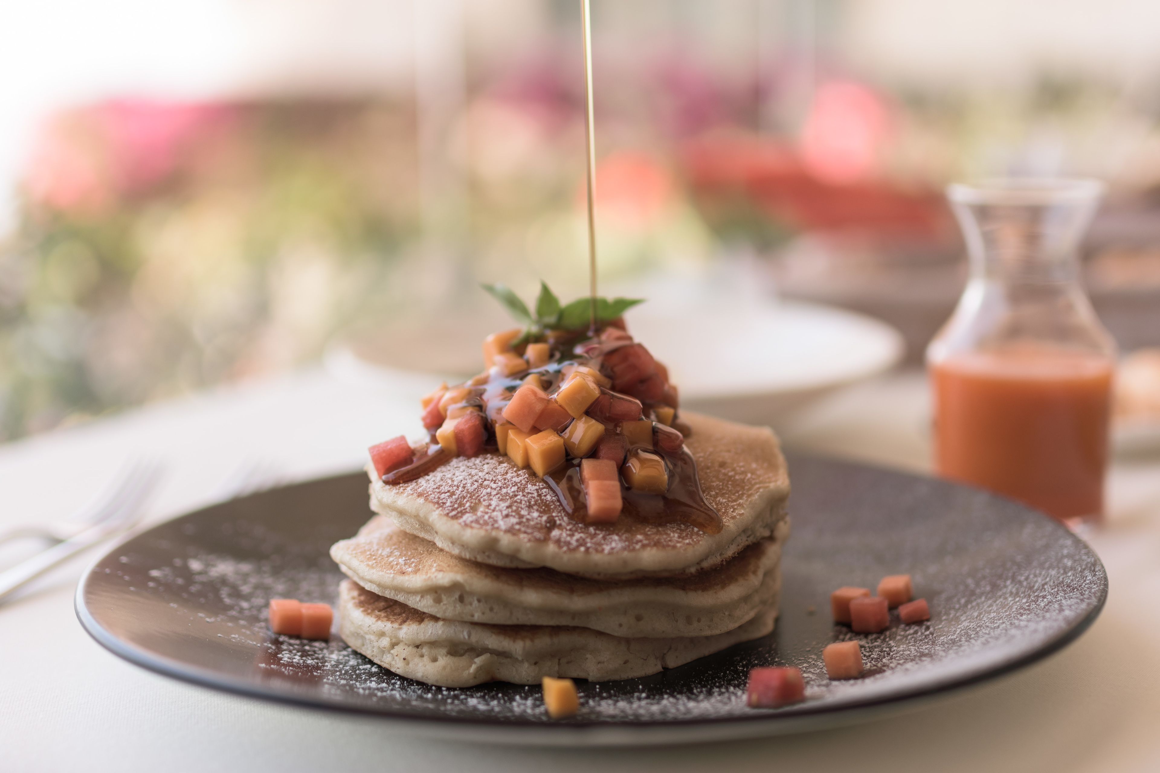 Lautasella on kasa pannukakkuja, päälle on kaadettu siirappia ja lisäksi siinä on kuutioitua kinkkua.