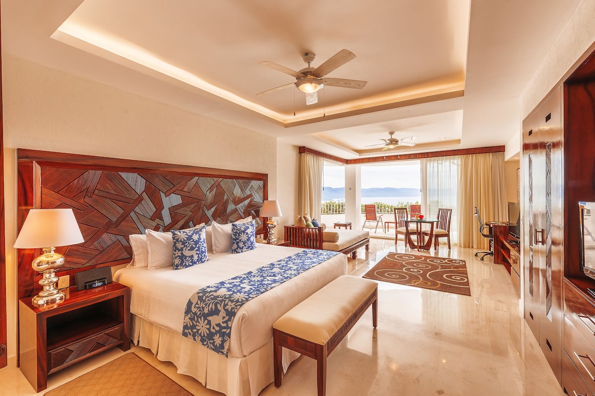 Habitación de hotel con una cama grande, un escritorio, una silla, un televisor y un balcón con vistas.