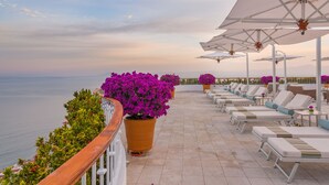Terraza frente al mar con tumbonas y sombrillas, con vistas al océano.