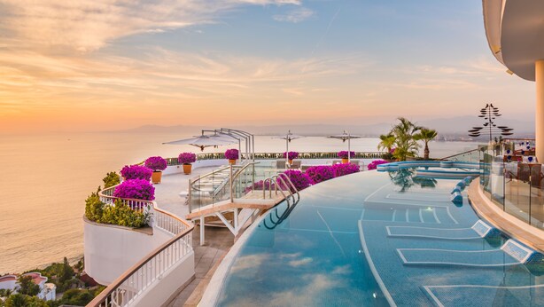 Vista de la piscina con cielo despejado, un atardecer y vista al mar.
