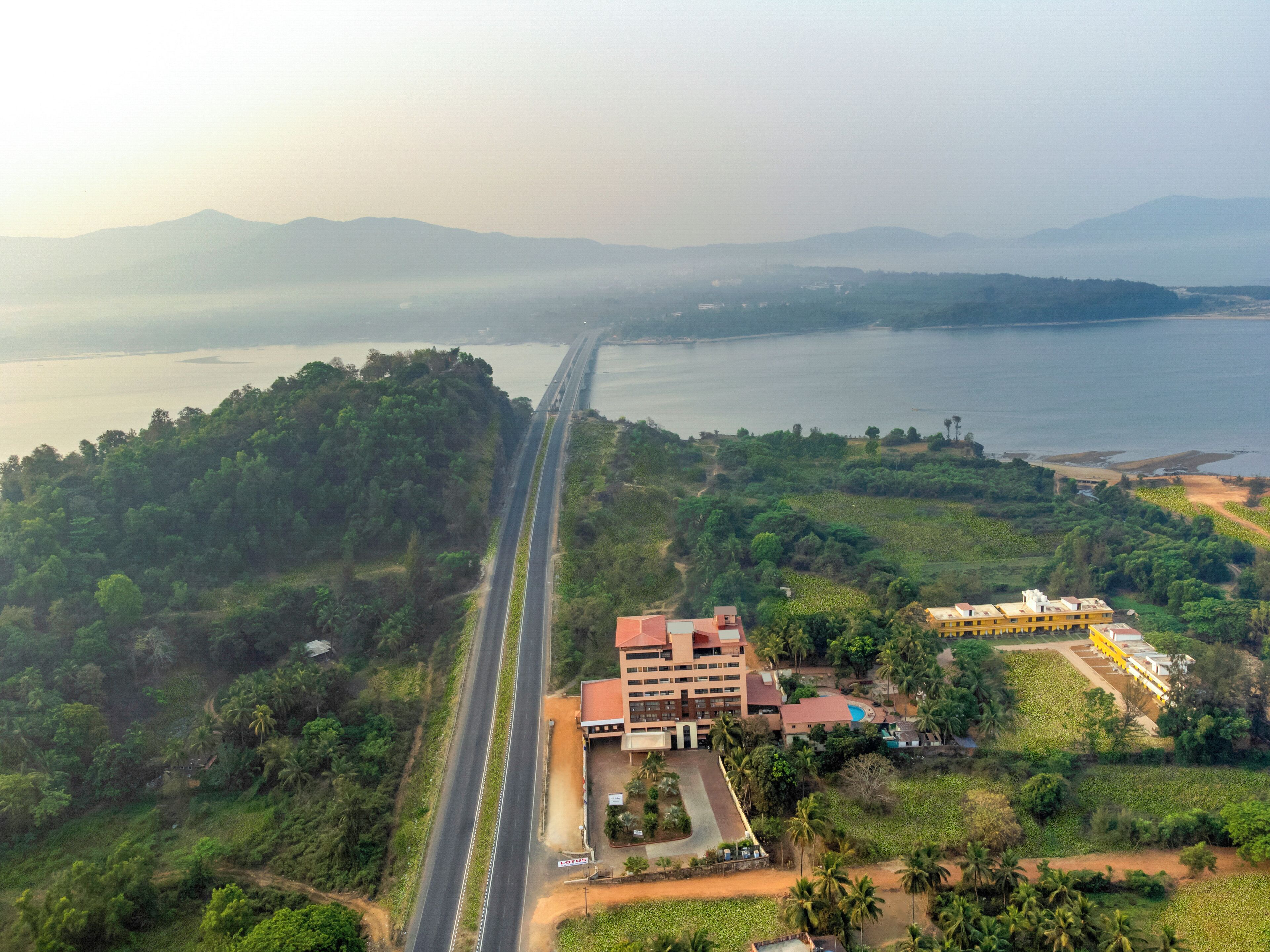 An aerial view of a coastal area with a bridge, lush greenery, and a hotel with multiple buildings.