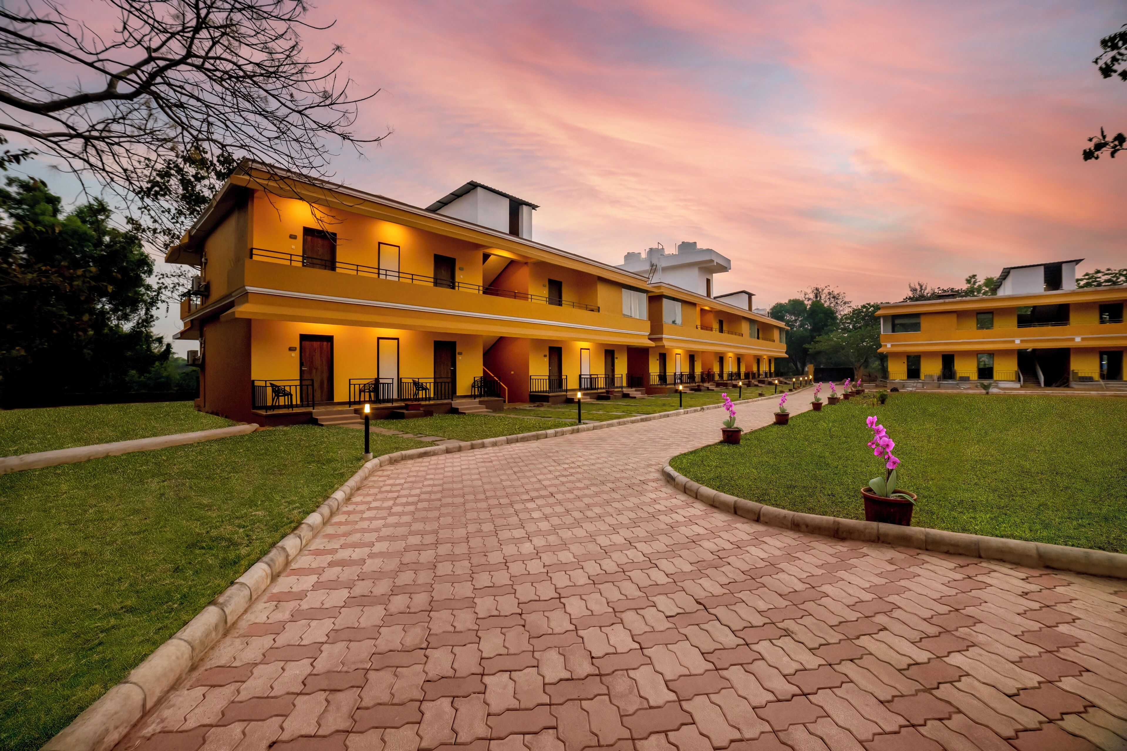 A multi-story hotel with a brick pathway leading to the entrance, surrounded by well-maintained lawns and potted plants.