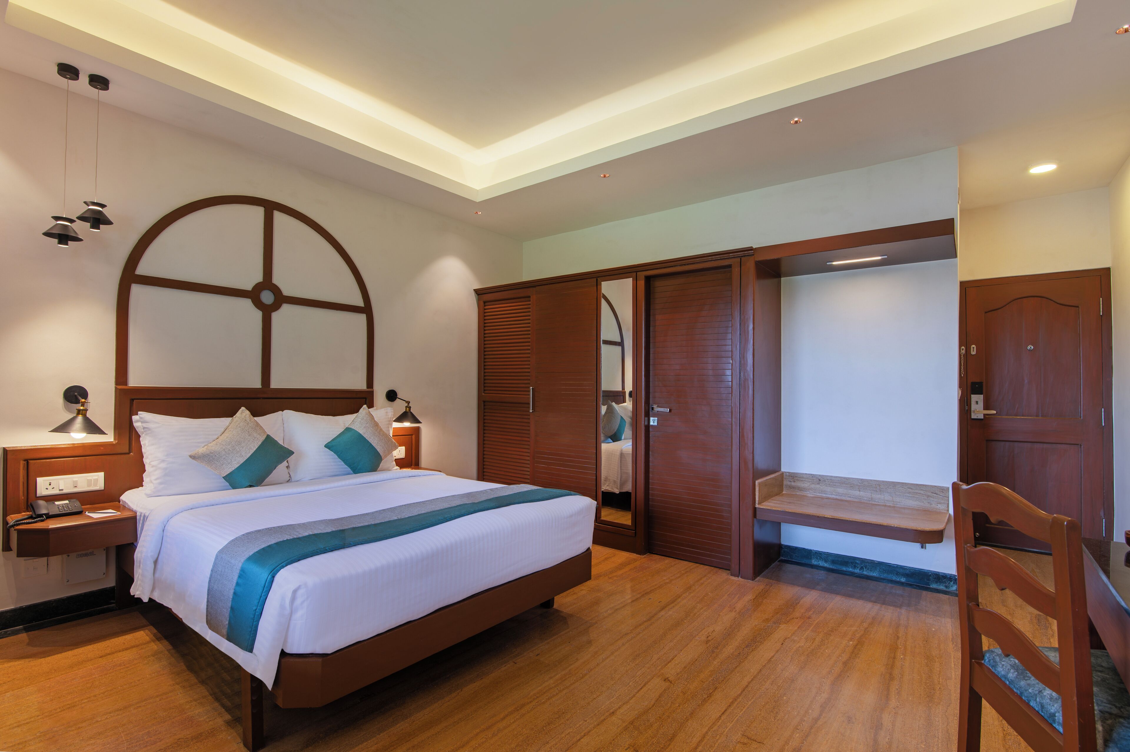 A well-lit bedroom with a large bed, wooden wardrobe, and a small bench.