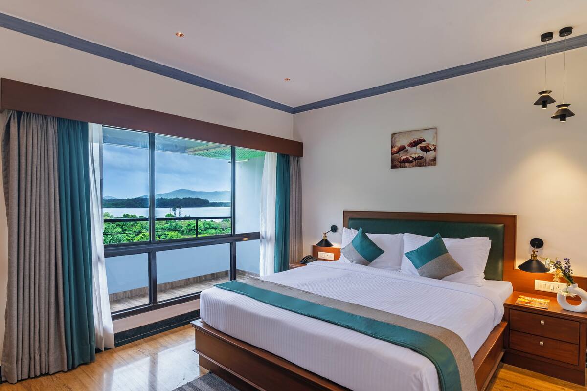 Quarto de hotel com uma cama grande, mesa de cabeceira, abajur e vista para um lago.