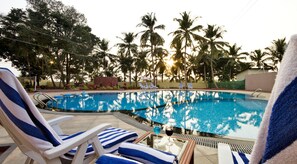 A swimming pool with lounge chairs and a glass table with drinks, surrounded by palm trees. - Sterling Karwar (Karwar)