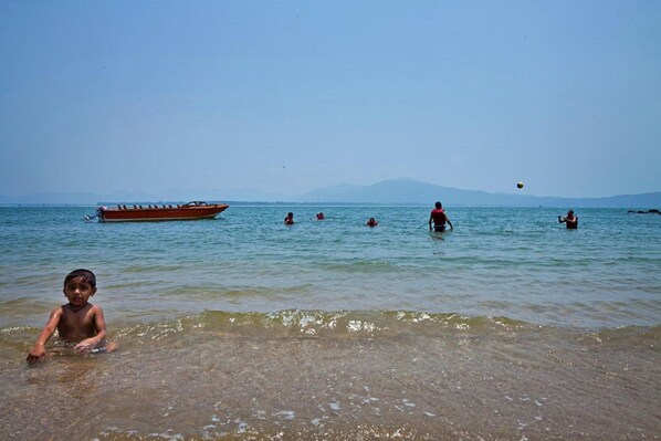 Una playa con agua cristalina, un bote y gente nadando.