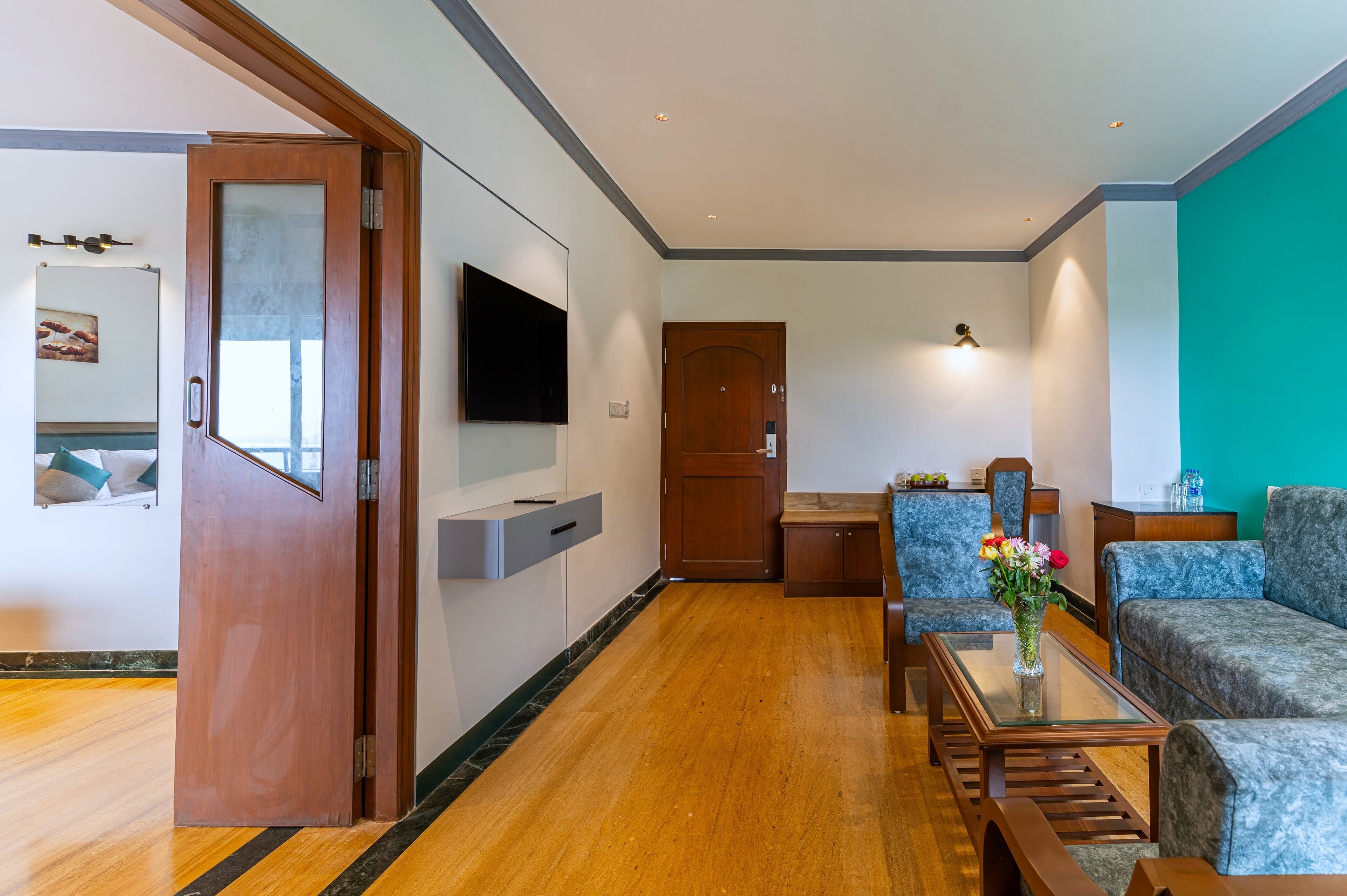 A modern living room with a wooden floor, a glass coffee table, a sofa, and a TV mounted on the wall.