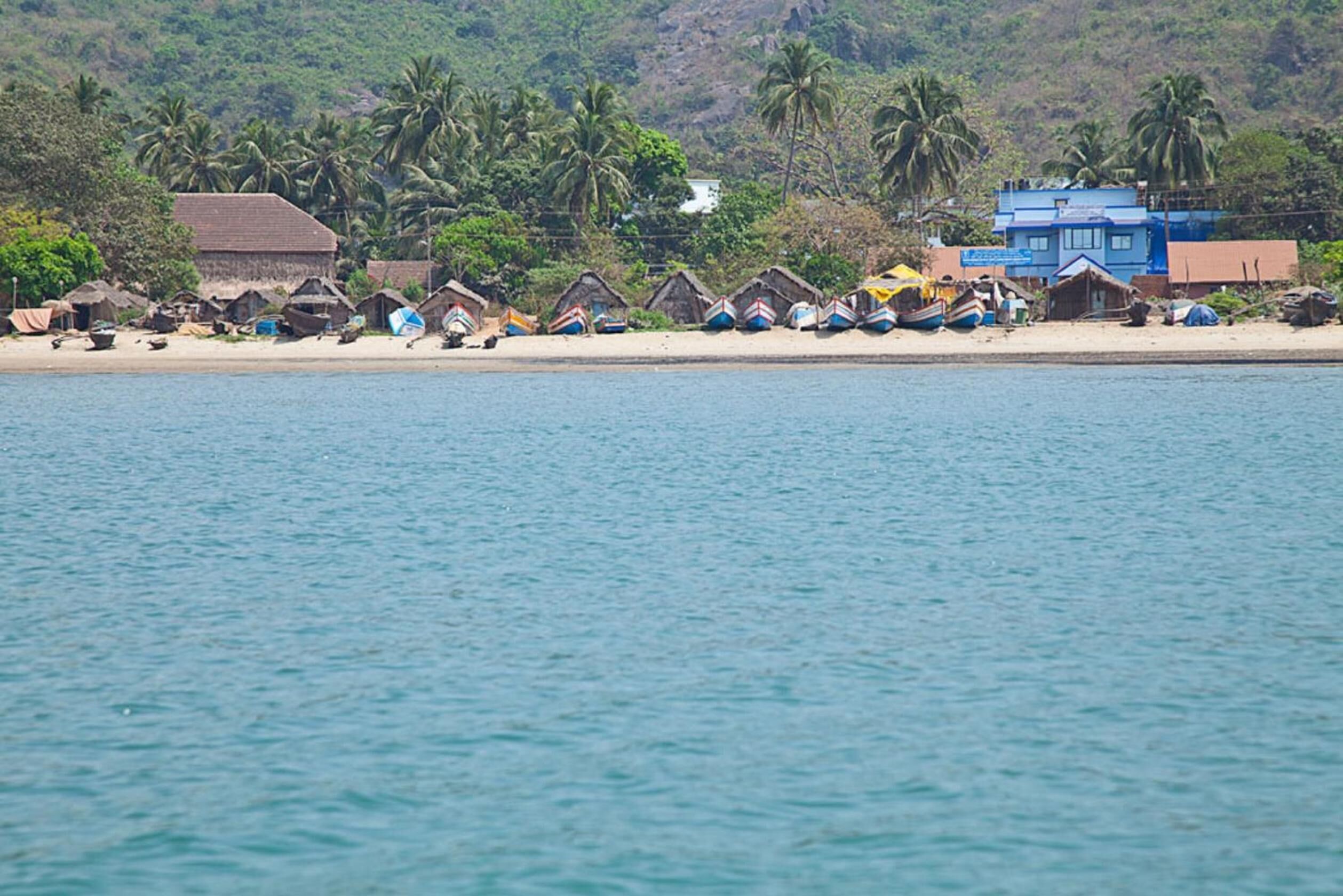 A beach with thatched-roof huts and a few modern buildings.