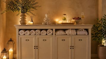 A cabinet with towels, a Buddha statue, candles, and a pitcher of water.