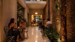 A corridor with a brick wall, plants, and a dining area with tables and chairs. - Duque Hotel Boutique & Spa (Buenos Aires)