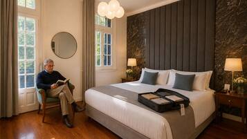 A hotel room with a large bed, a reading chair, a round mirror, and a window with curtains.