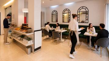 Un café moderno con servicio de buffet, una zona de estar y una barra donde un camarero atiende a los clientes.