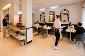 A modern cafe with a buffet, seating area, and a counter where a server is attending to guests. - Duque Hotel Boutique & Spa (Buenos Aires)