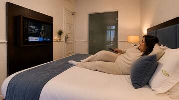 A hotel room with a bed, a TV mounted on the wall, a door, and a lamp.
