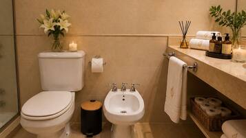 A bathroom with a toilet, bidet, and sink, framed artwork on the wall, and toiletries on the counter.