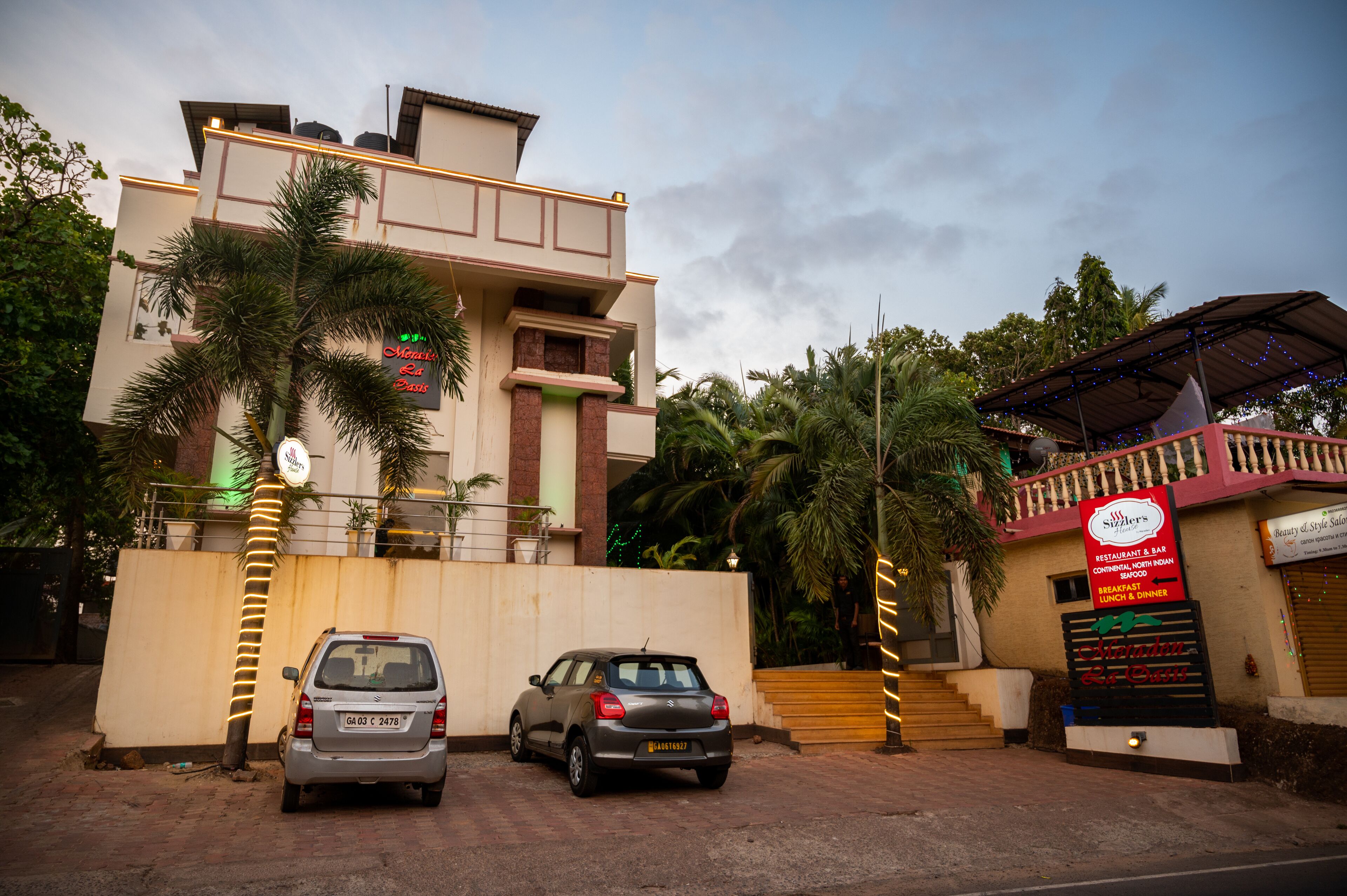 Un edificio con un letrero que dice 'Monaco Eat Place' y otro para 'Sizzler's Restaurant & Bar'. Hay dos coches estacionados adelante.