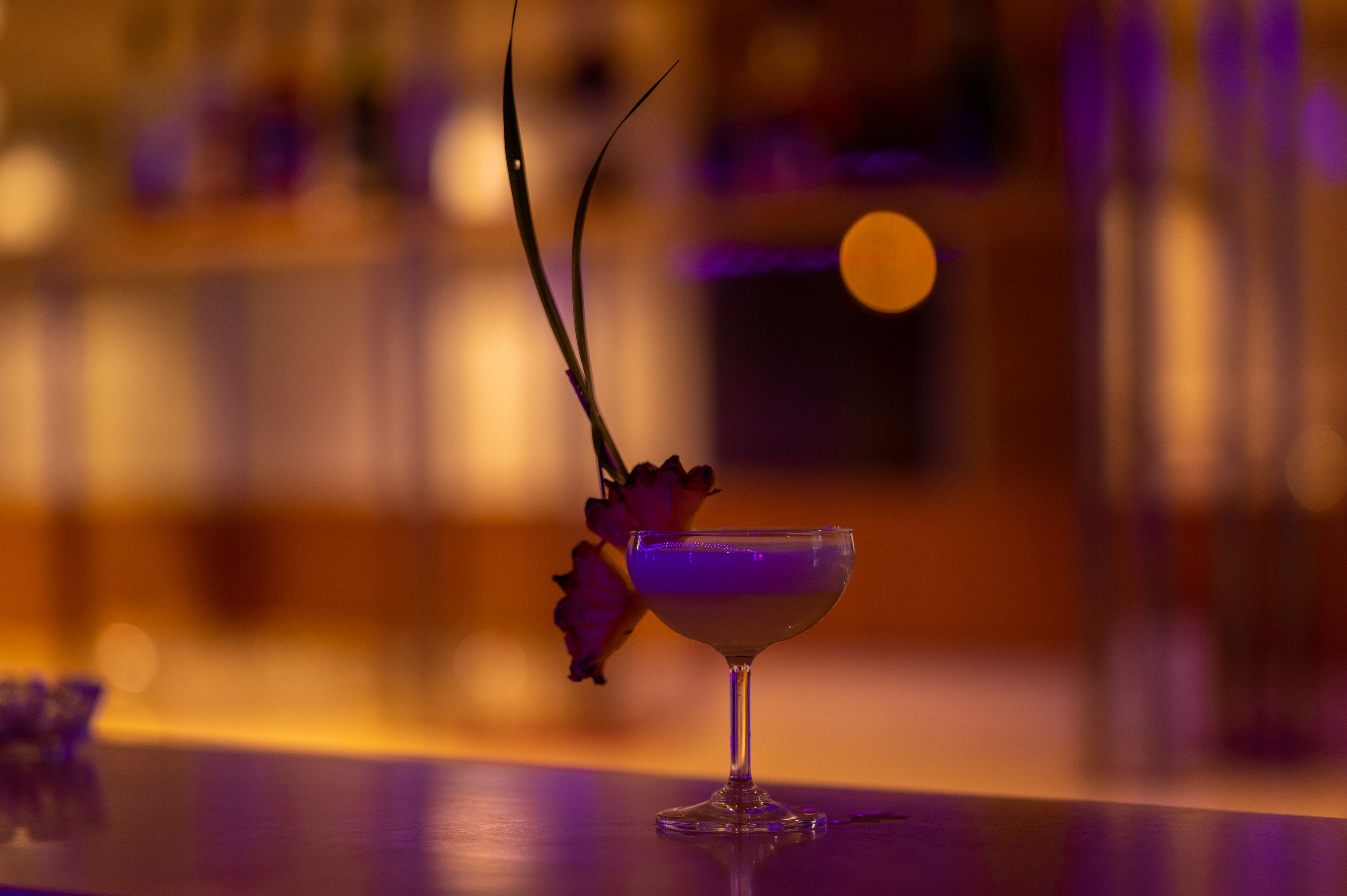 A cocktail glass with a decorative flower on a bar counter.