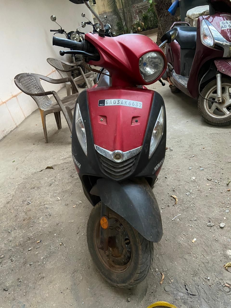 A red scooter parked on a concrete surface with a license plate visible.