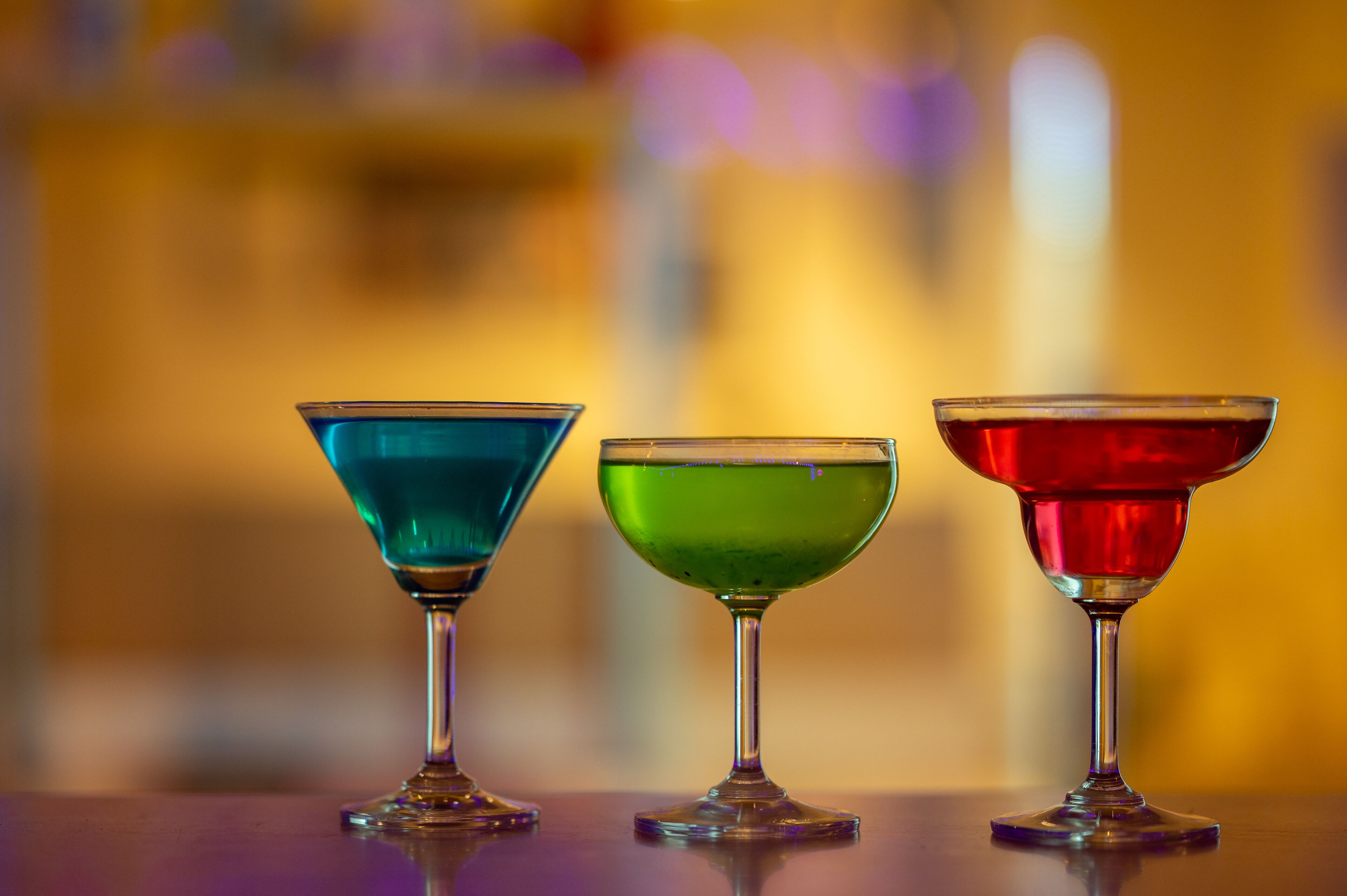 Three cocktail glasses on a reflective surface with a blurred background.