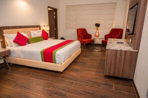 A hotel room with a bed, two red chairs, a small table, and a TV. - La Oasis by Meraden (Anjuna)