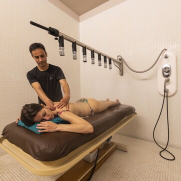 A massage therapy room with a massage table, a massage therapist, and a wall-mounted shower system.