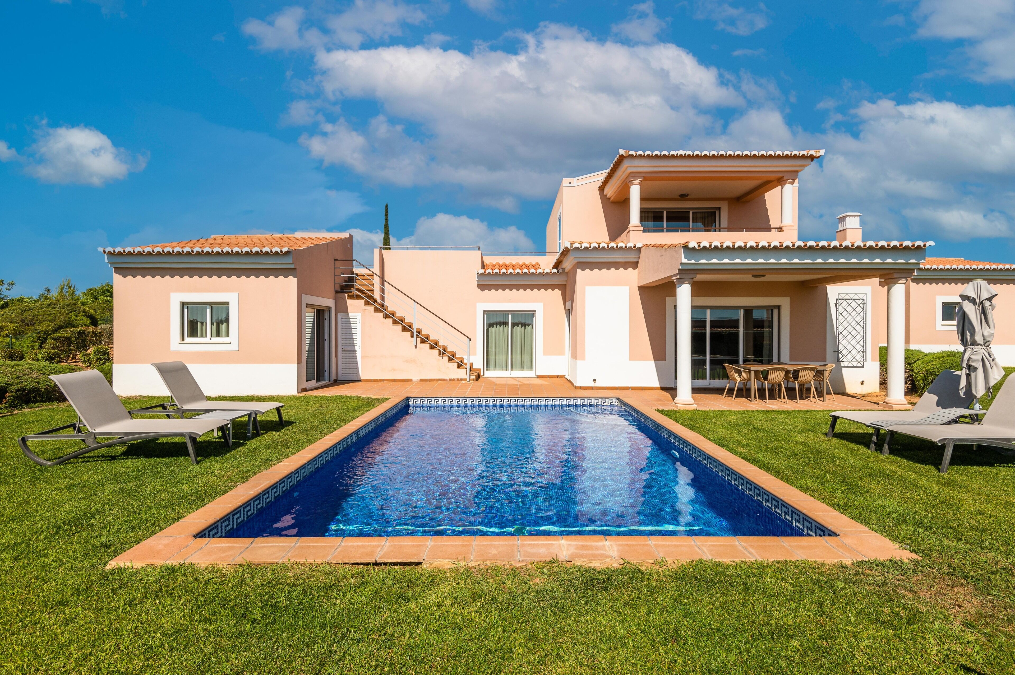 A two-story house with a swimming pool, outdoor seating, and a staircase leading to the upper floor.