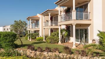 A multi-story residential building with balconies, a landscaped garden, and a small pond.