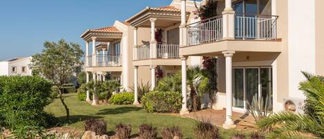 A multi-story residential building with balconies, a landscaped garden, and a small pond.