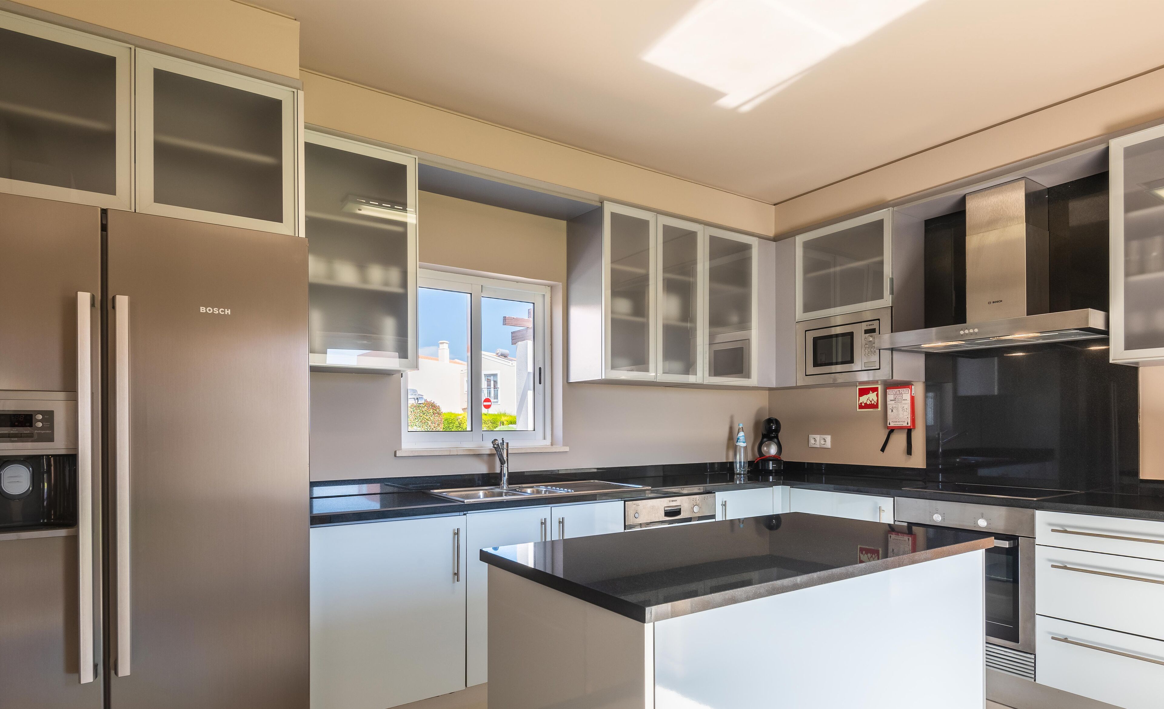 A modern kitchen with white cabinets, a black countertop, and stainless steel appliances including a refrigerator, oven, and microwave.