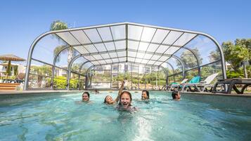 A swimming pool with a glass enclosure, surrounded by lounge chairs and palm trees.