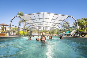 Una piscina con cerramiento de vidrio, rodeada de sillas de descanso y palmeras.