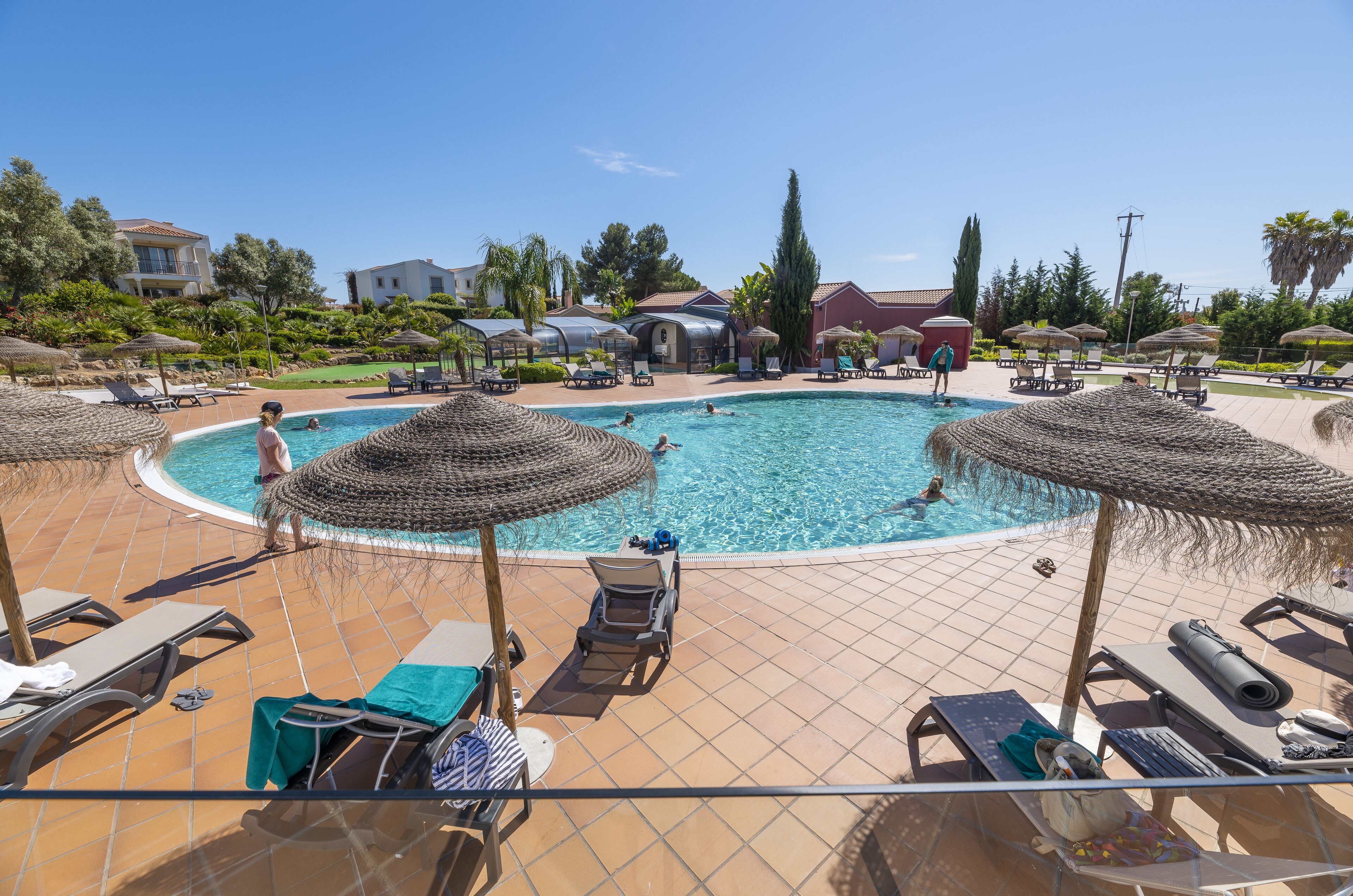 Un espace piscine aménagé avec des chaises longues, des parasols et une piscine à l’eau d’un bleu cristallin.