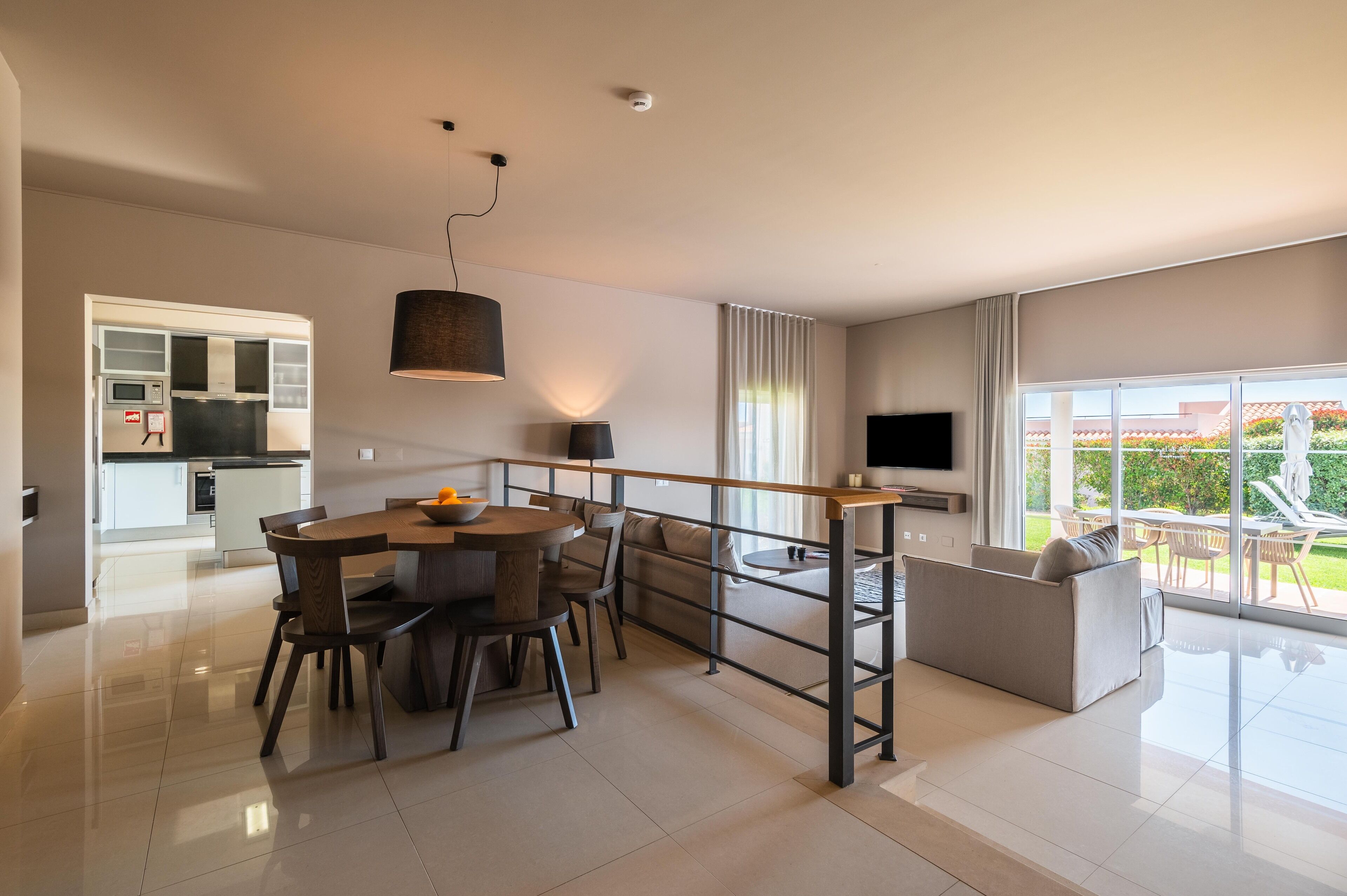 Una sala de estar moderna con comedor, sofá, televisor y un balcón con mobiliario exterior.