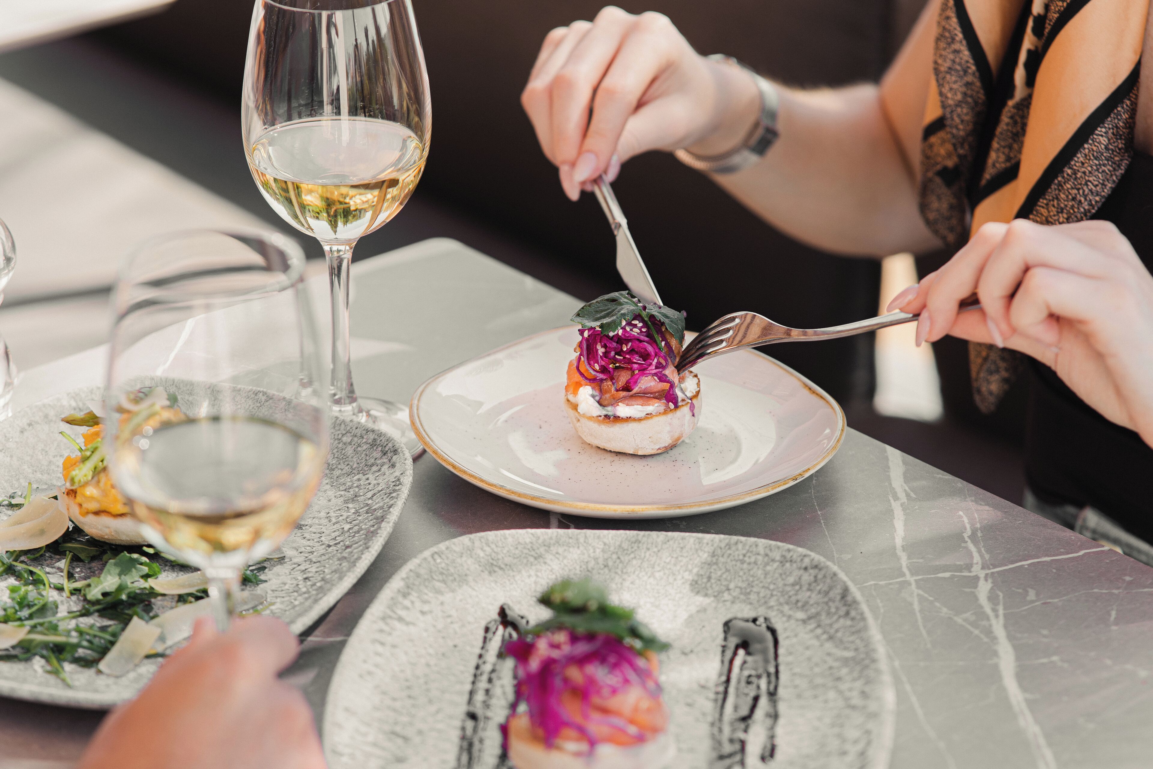 Una mesa de comedor con platos de comida y una copa de vino blanco.