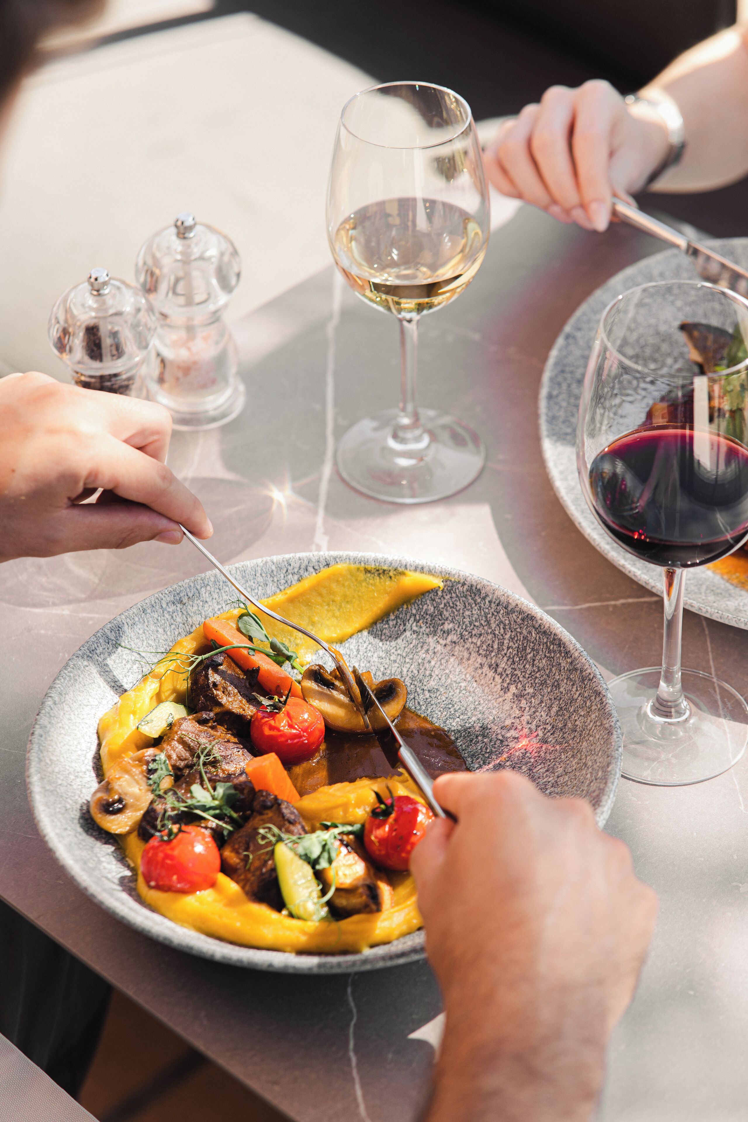 Una mesa de comedor con un plato de comida, una copa de vino y saleros y pimenteros.