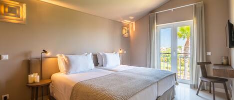 A hotel room with a large bed, a desk, and a balcony with a view of palm trees.