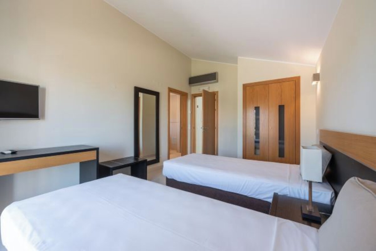 A hotel room with two beds, a desk, a TV, and a mirror.