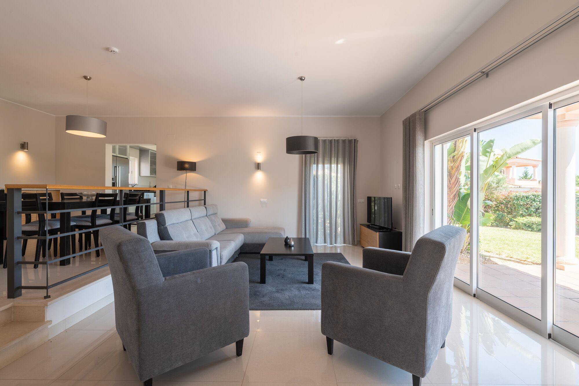 Een moderne woonkamer met een bank, twee fauteuils, een salontafel en een eethoek met stoelen en een tafel.