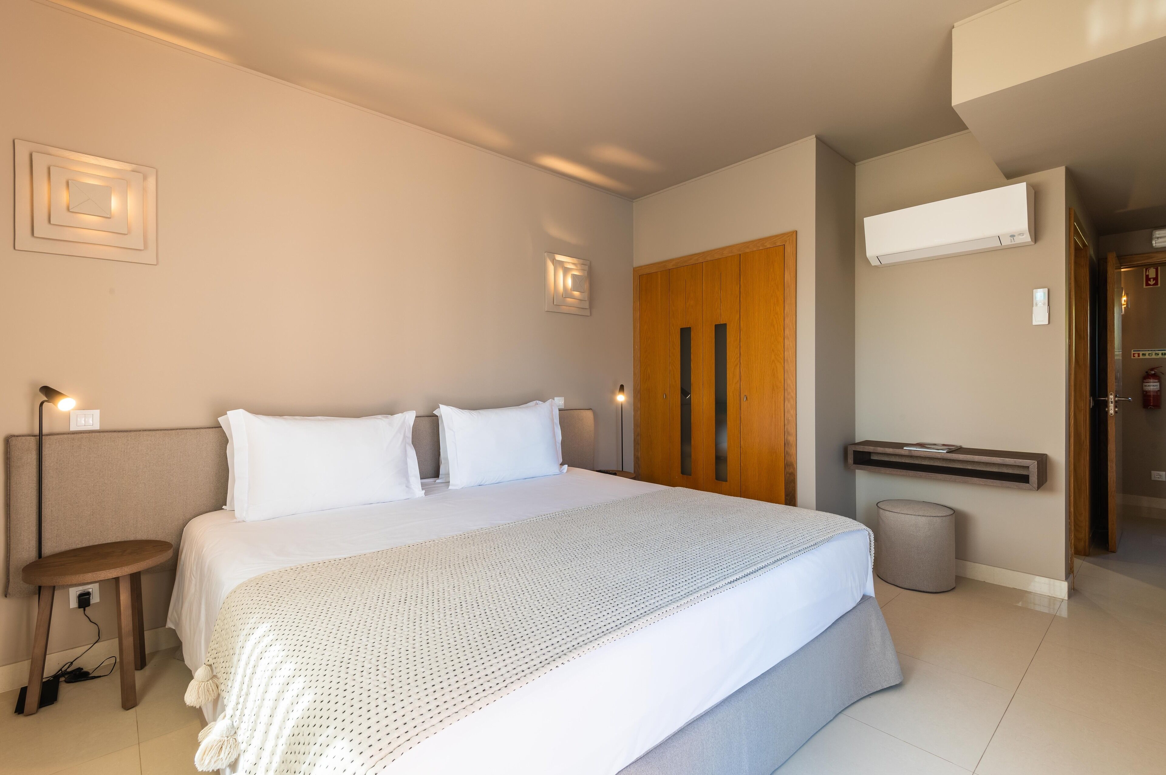 Une chambre d’hôtel moderne, dotée d’un grand lit, d’une petite table, d’une poubelle et d’une porte donnant sur une autre pièce.