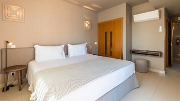 Une chambre d’hôtel moderne, dotée d’un grand lit, d’une petite table, d’une poubelle et d’une porte donnant sur une autre pièce.
