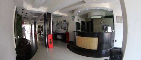 A modern reception area with a curved black reception desk, a wooden accent, and a wall-mounted TV.