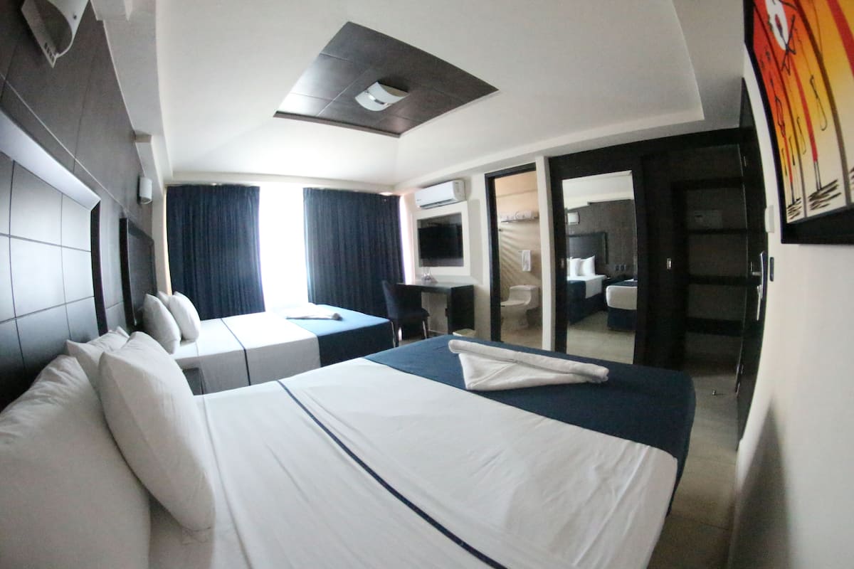 Habitación de hotel con una cama grande, un escritorio, una silla y un baño visible a través de una puerta abierta.