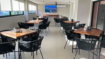 Un salón de conferencias con varias mesas y sillas, un televisor de pantalla plana grande en la pared y vistas al exterior a través de las ventanas.