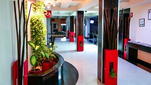 A modern hotel lobby with a curved reception desk, potted plants, and a car parked in the background. - Hotel Portonovo Plaza Malecón (Puerto Vallarta)