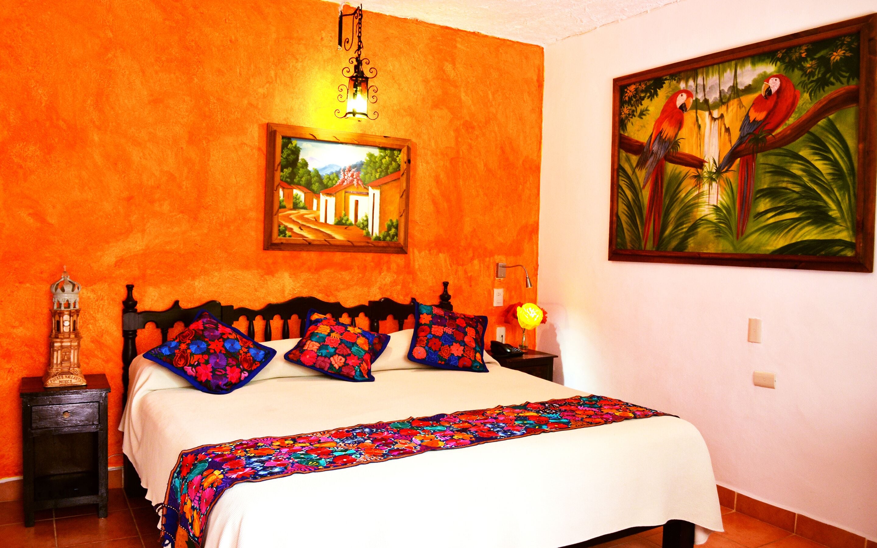 A bedroom with a bed, a nightstand, a lamp, a painting, and a decorative item on the nightstand.