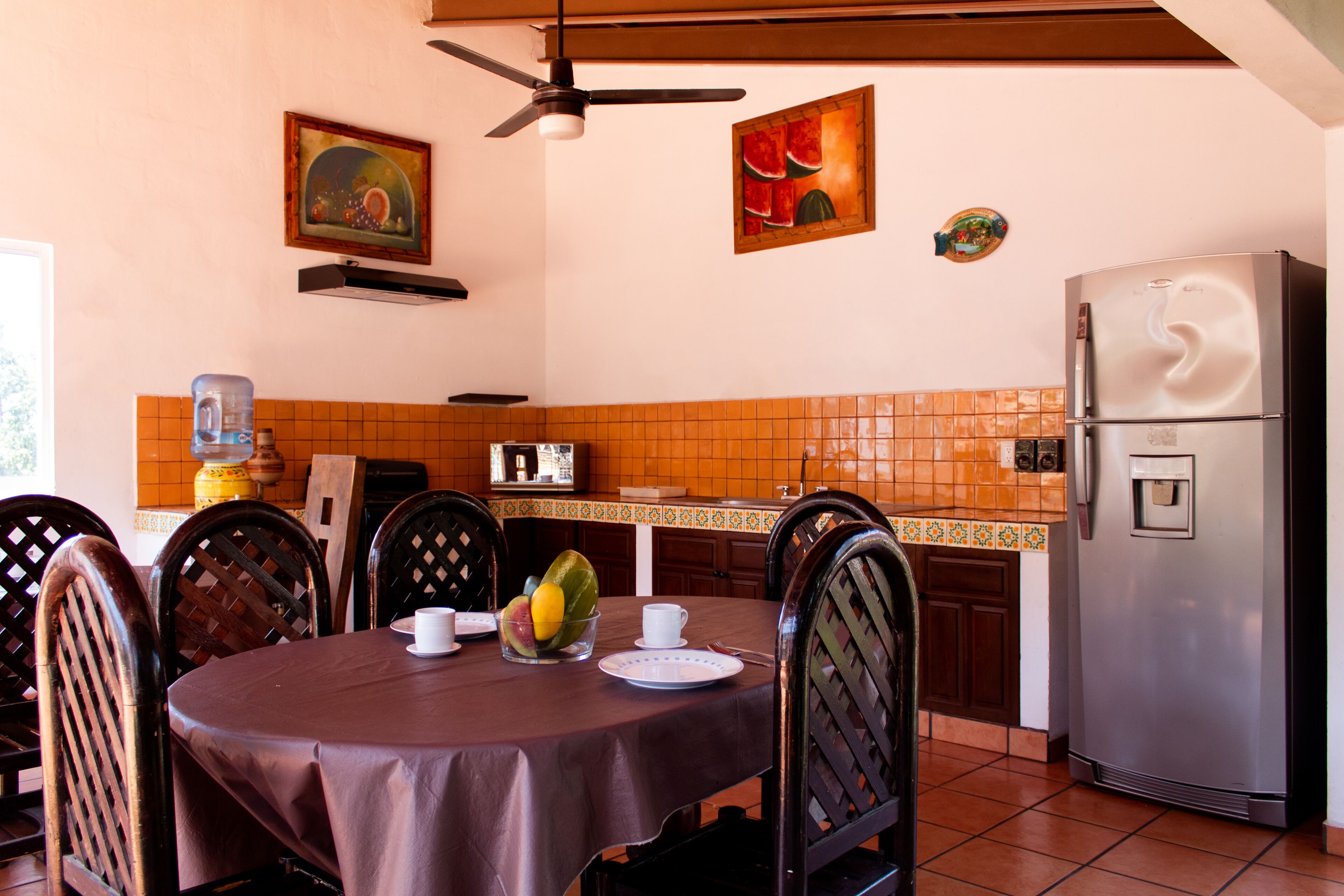 Comedor con mesa para dos, sillas, refrigerador y electrodomésticos de cocina.