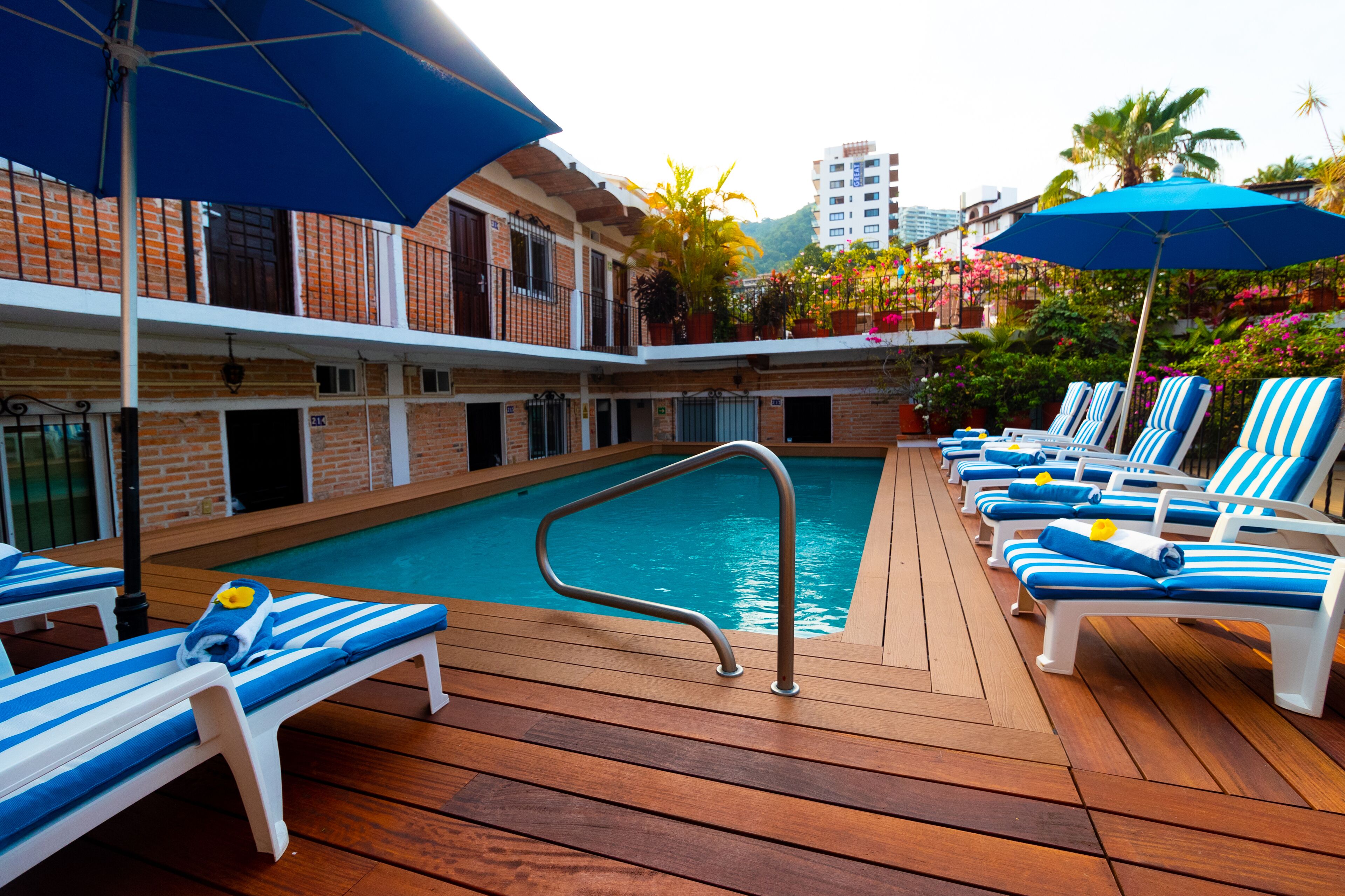 A poolside area with lounge chairs and umbrellas, a pool, and a building with balconies.