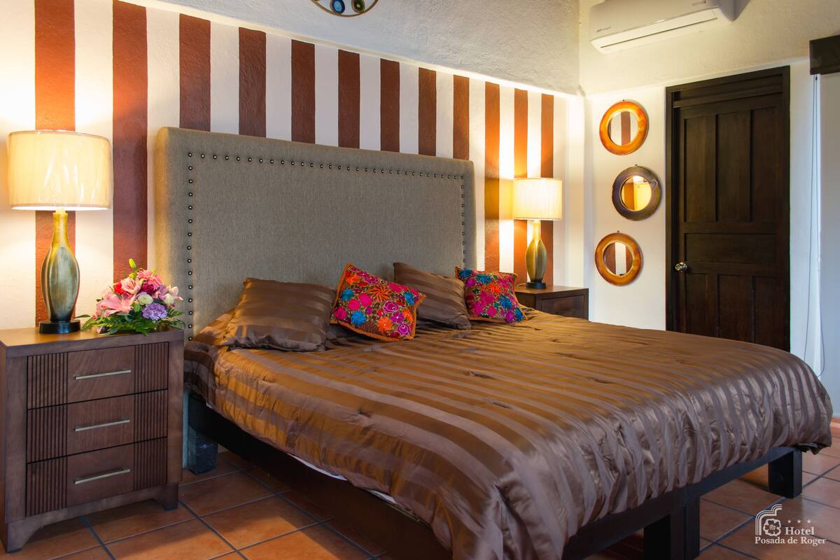 A hotel room with a large bed, striped wall, and decorative mirrors.