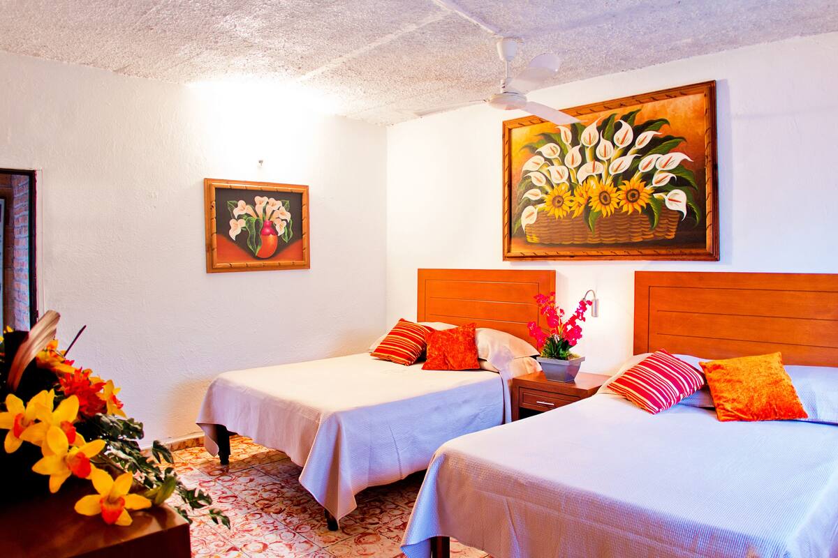 A hotel room with two beds, a wooden headboard, a nightstand, and a wall with two paintings.