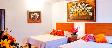 A hotel room with two beds, a wooden headboard, a nightstand, and a wall with two paintings.